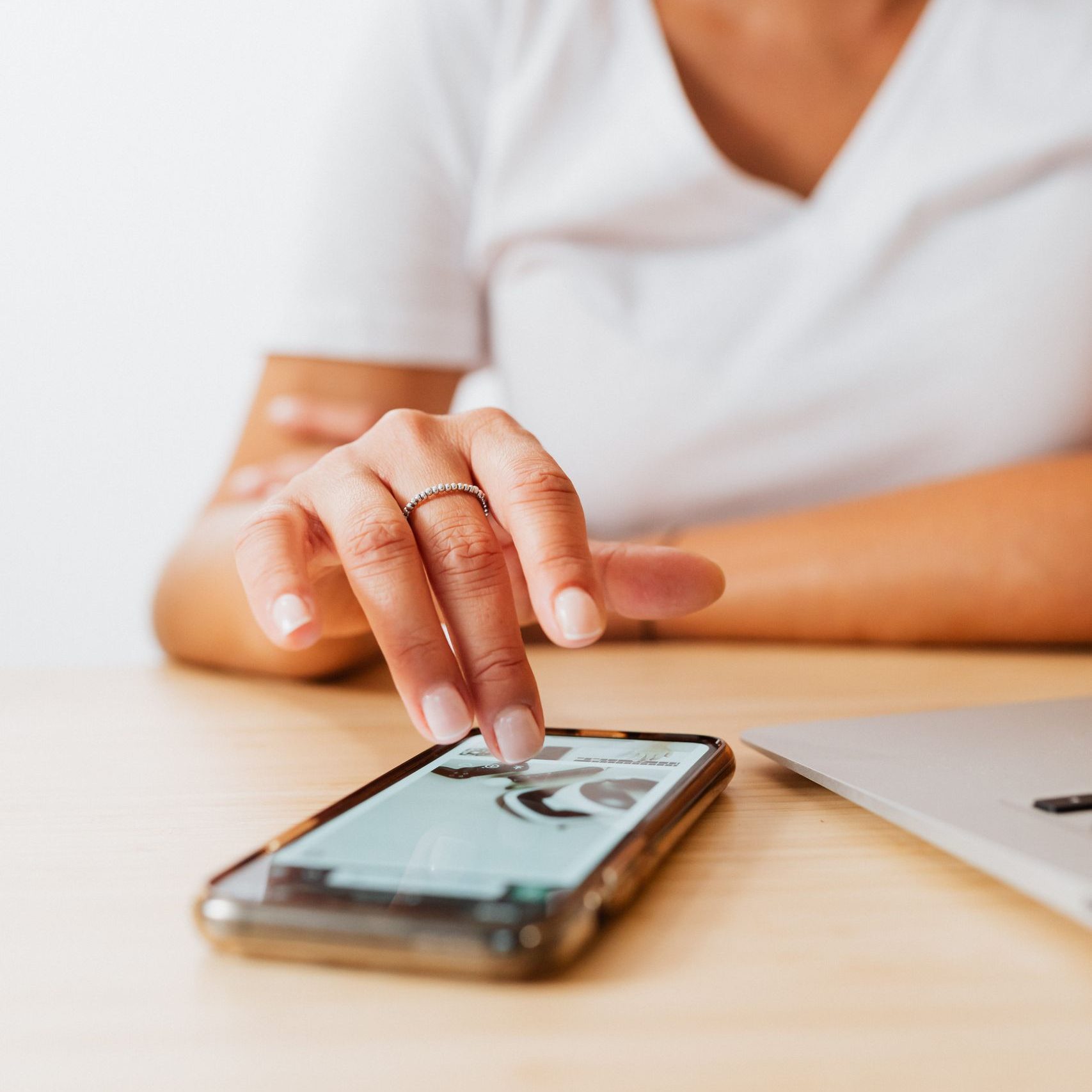 Close-up of a woman operating a smartphone at a wooden desk with a laptop, showcasing modern technology use.